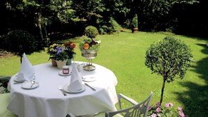 Una mesa redonda al aire libre, cubierta con un mantel blanco, rodeada de sillas y una pequeña planta en maceta con flores.