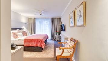 Ein Hotelzimmer mit Bett, Schreibtisch, Sessel, Fernseher und zwei gerahmten Bildern an der Wand.