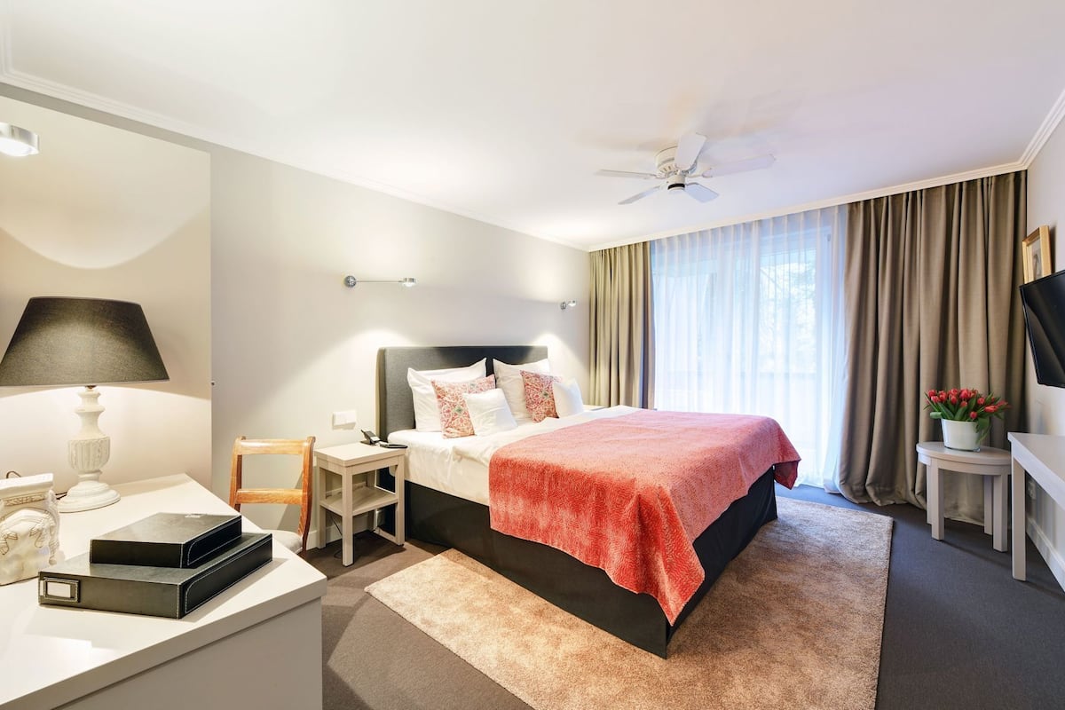 A hotel room with a bed, bedside table, lamp, TV, and curtains.