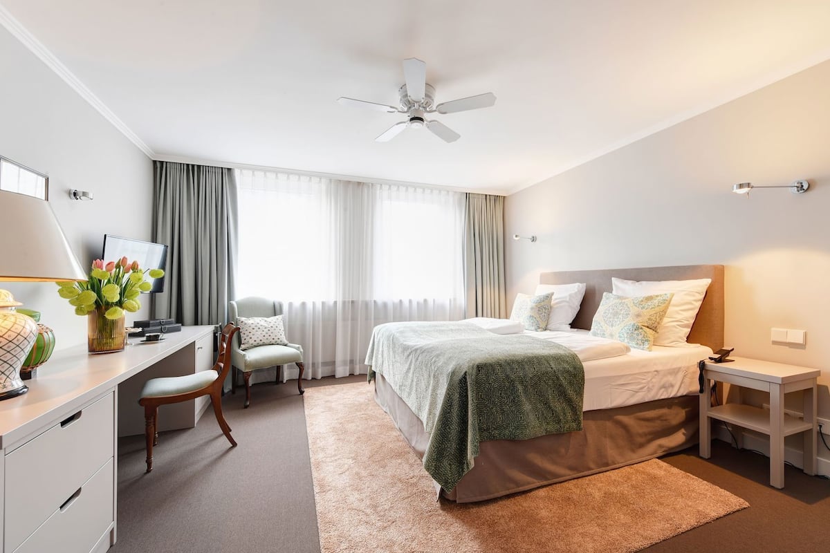 A hotel room with a bed, desk, chair, and a ceiling fan.