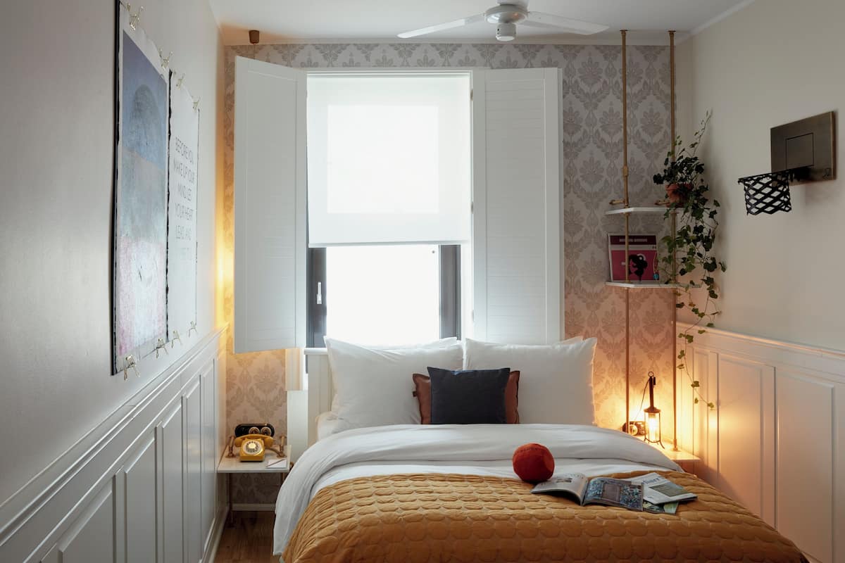 A bedroom with a bed, a nightstand, a window, a ceiling fan, and a wall-mounted shelf.
