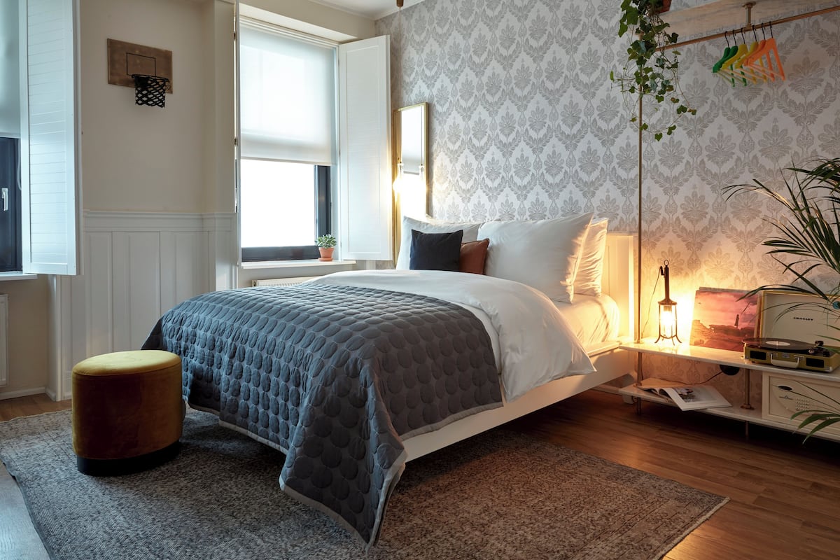 A bedroom with a bed, bedside table, lamp, and a window.