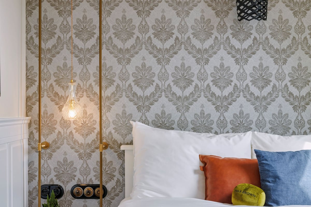 A neatly made bed with a quilt, pillows, and a bedside table with a lamp and a book.