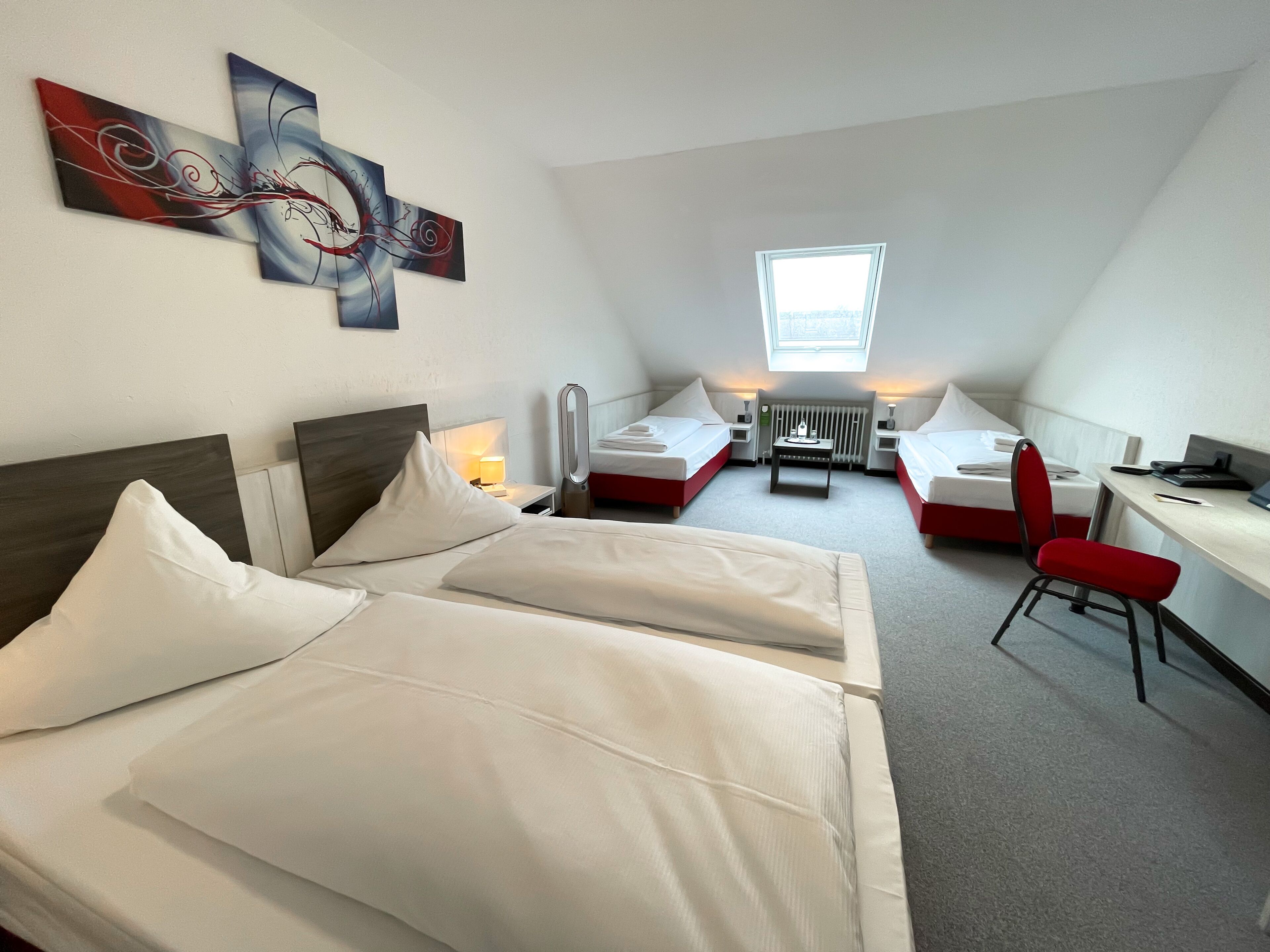 A hotel room with two beds, a desk, a chair, and a radiator.