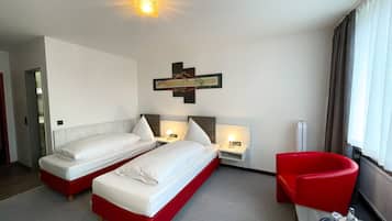 A hotel room with two beds, a red armchair, a small table with glasses, and a ceiling light.