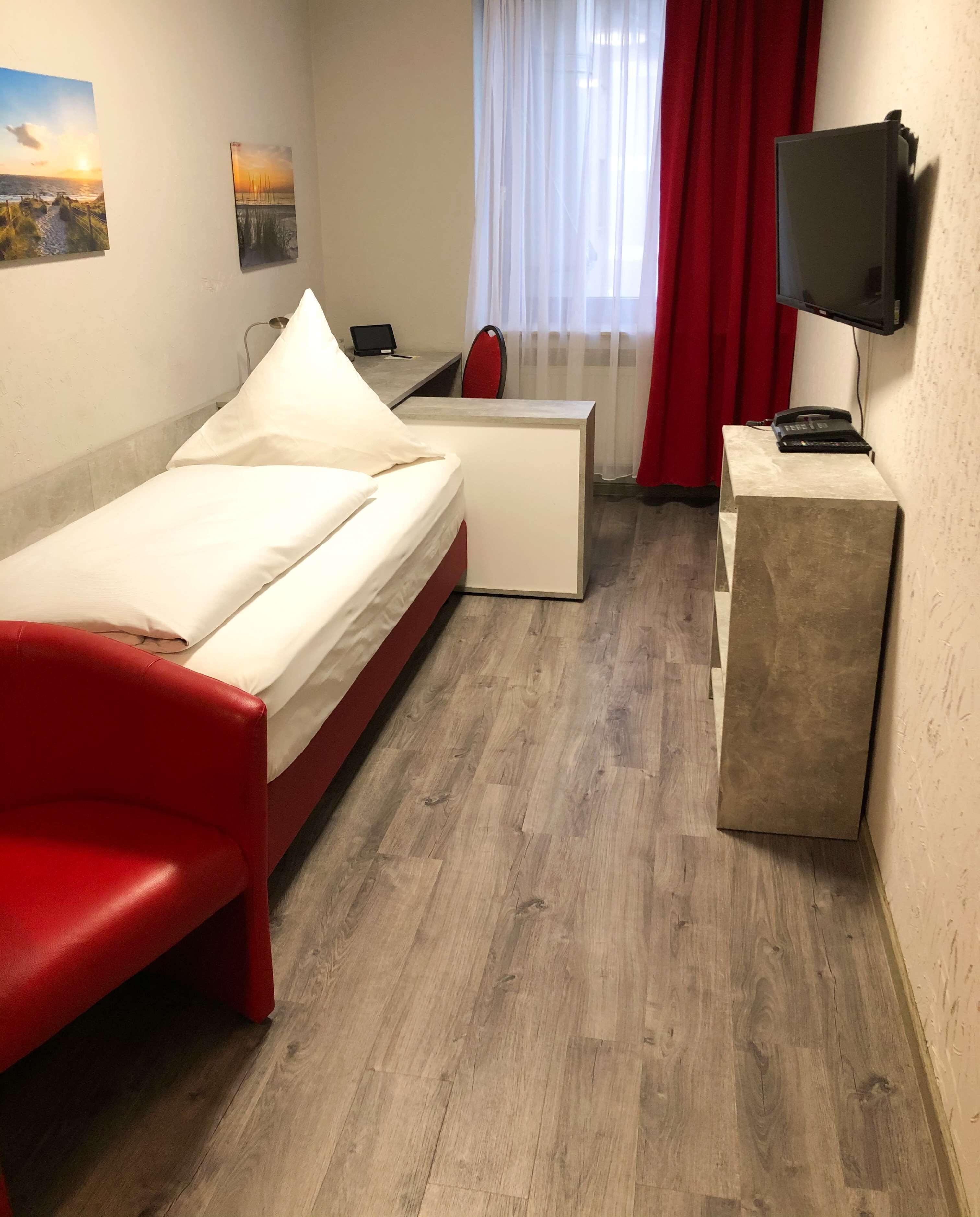 Una habitación de hotel con cama, escritorio, silla, televisor y obras de arte en las paredes.