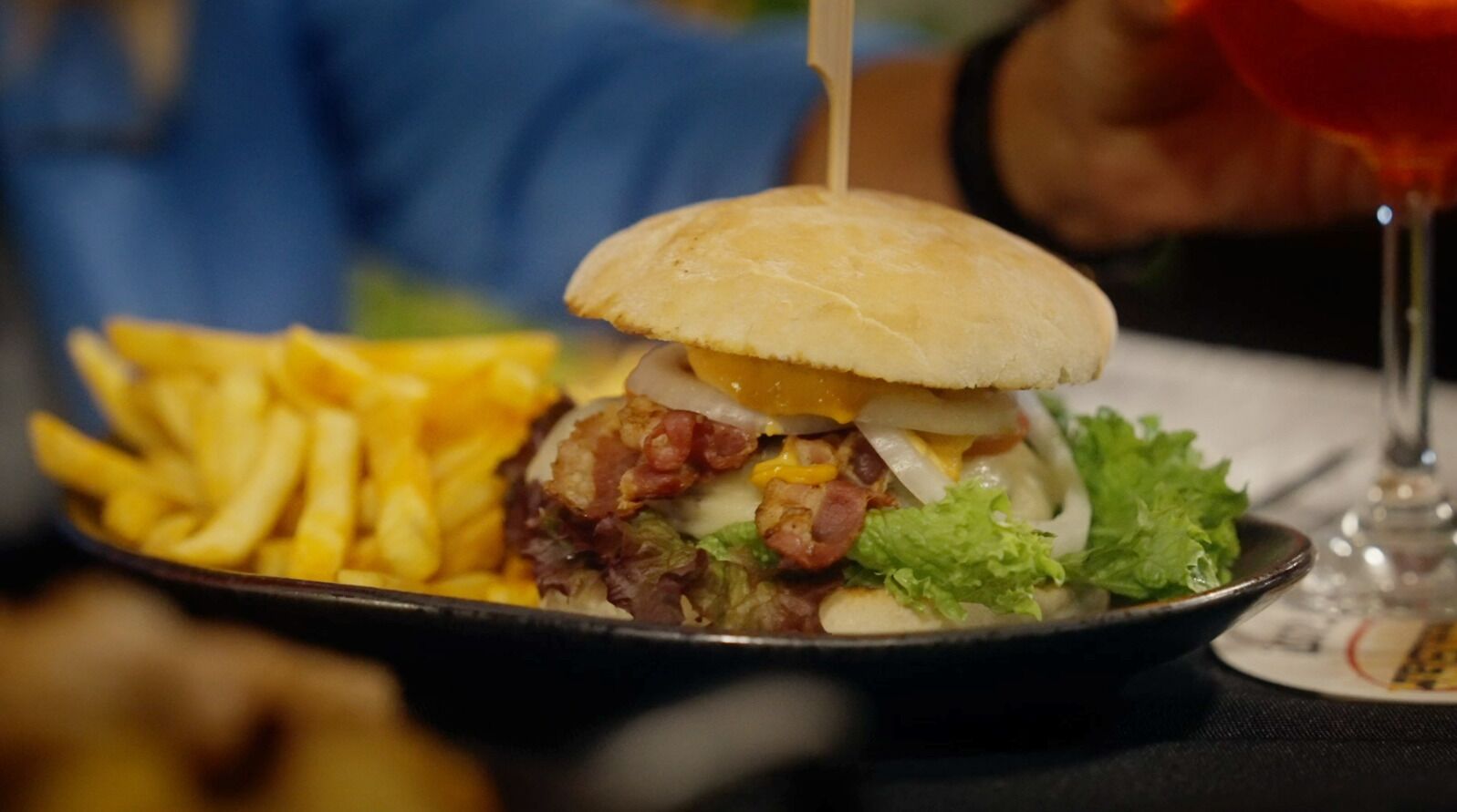 Een hamburger met friet en een drankje op een tafel.