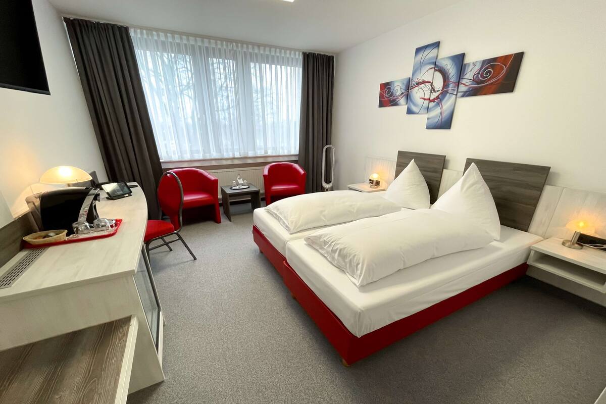 A hotel room with a bed, a desk, a chair, a small table, and a window with curtains.
