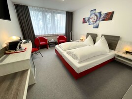 Habitación de hotel con cama, escritorio, silla, una mesita y ventana con cortinas.