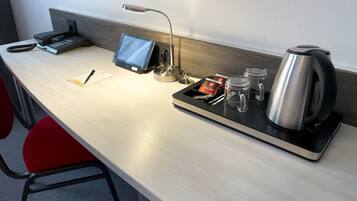 Ein Hotel-Schreibtisch mit Telefon, Tablet, Lampe, Teeservice und Gläsern.