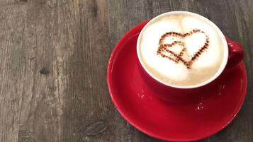 Una taza de café con un dibujo de corazón en espuma de leche sobre un platito rojo, sobre una mesa de madera.