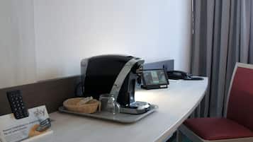 A hotel room with a desk featuring a coffee machine, a remote control, a tablet, and a Sky service sign.