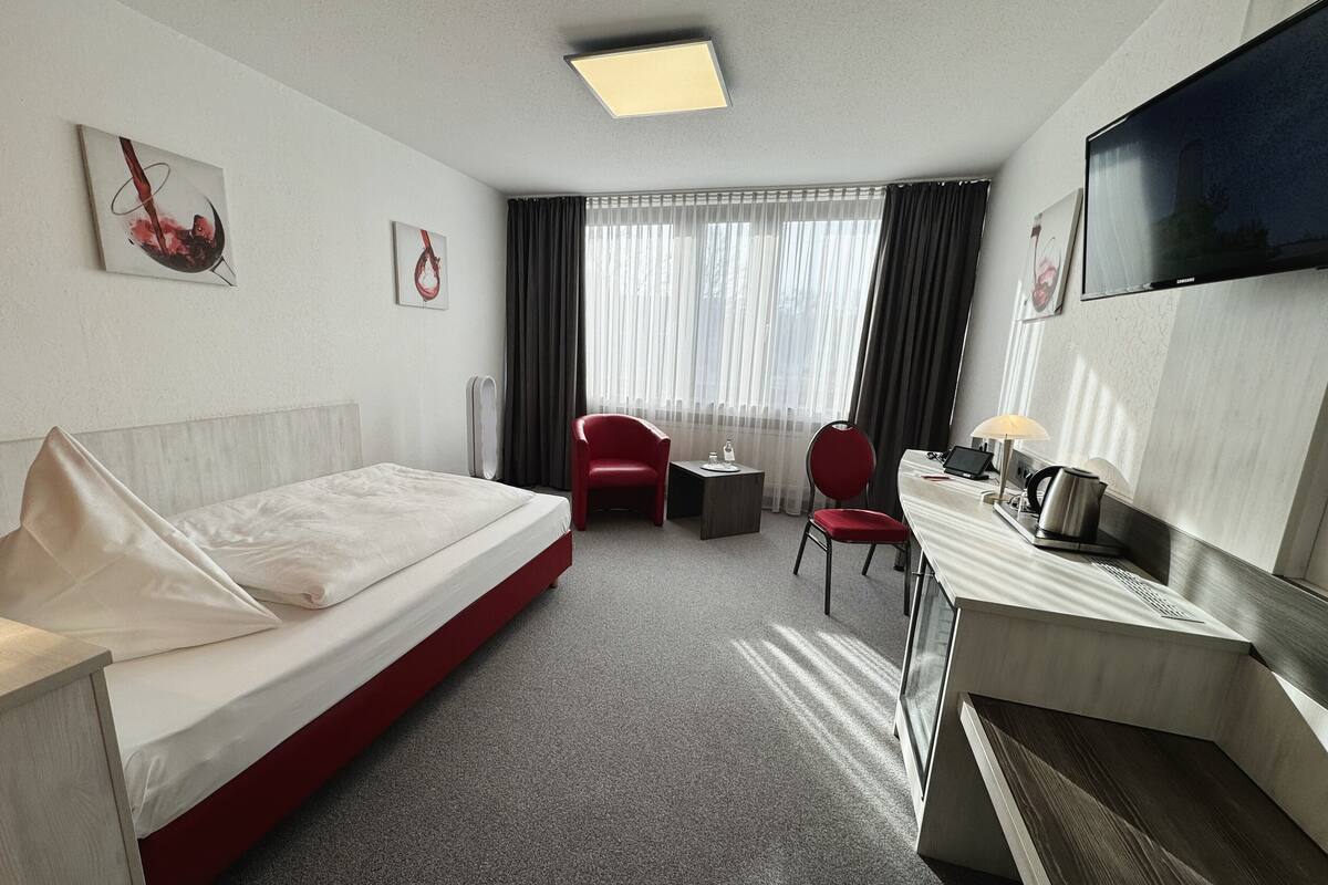 A hotel room with a bed, a desk with a chair, a TV, and artwork on the walls.