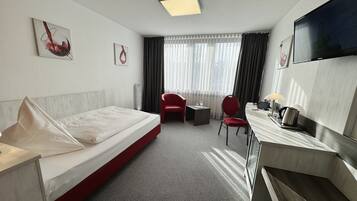 Una habitación de hotel con cama, escritorio con silla, televisor y obras de arte en las paredes.