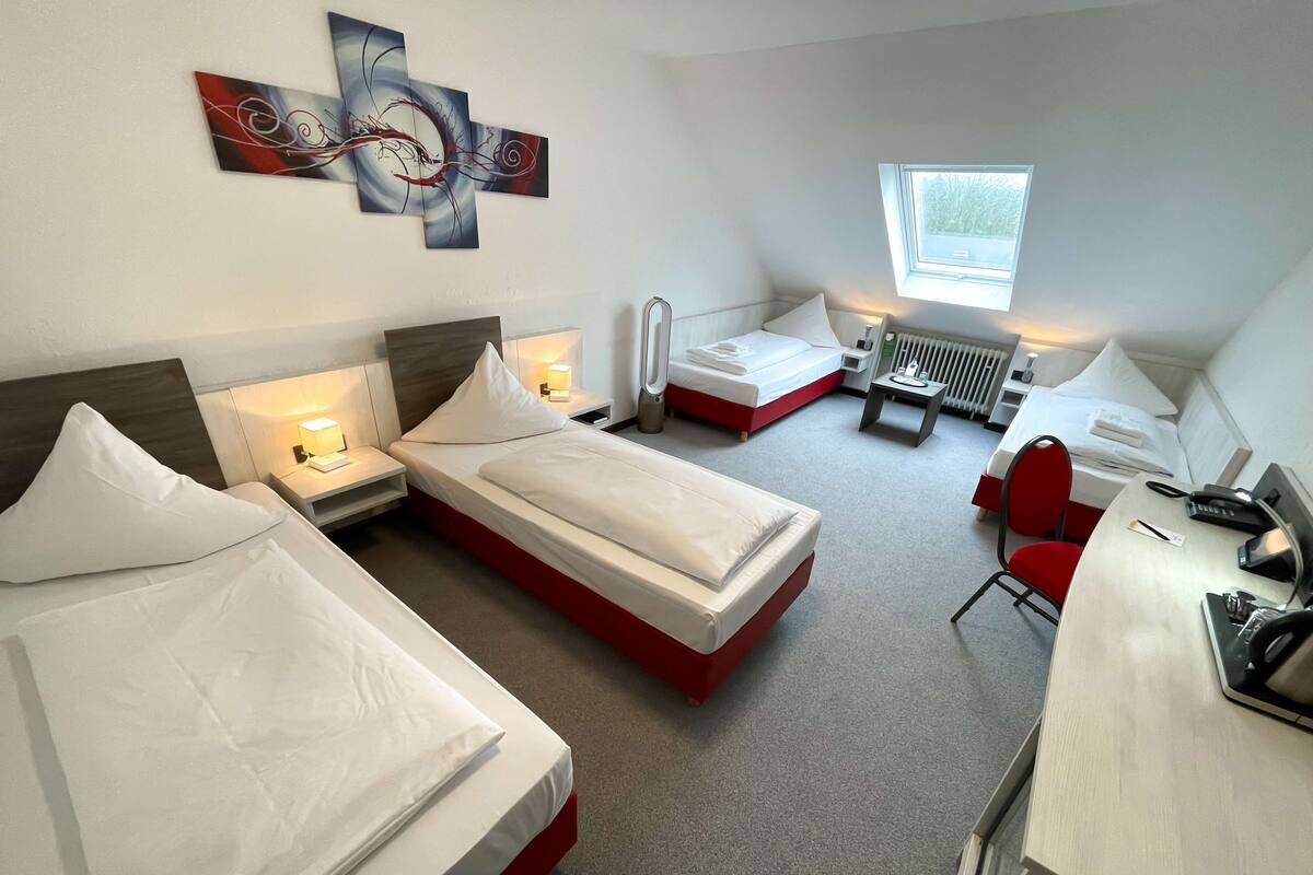 A hotel room with two beds, a desk, a chair, and a window.