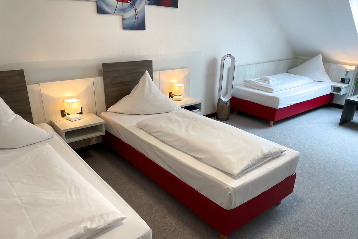 A hotel room with two single beds, each with a nightstand, a lamp, and a wall-mounted heater.