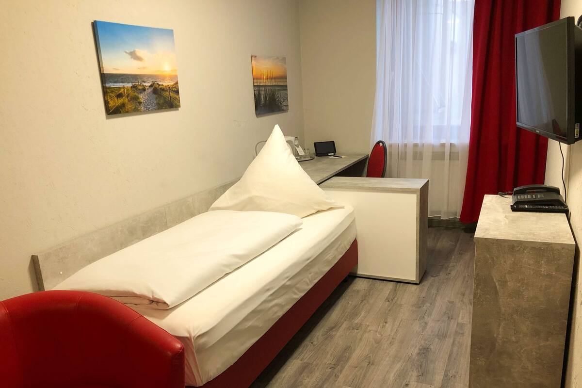 A compact hotel room with a bed, a desk, a chair, and a TV.