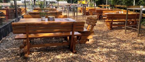 Un espacio al aire libre con bancos y mesas de madera, rodeado de árboles y edificios.