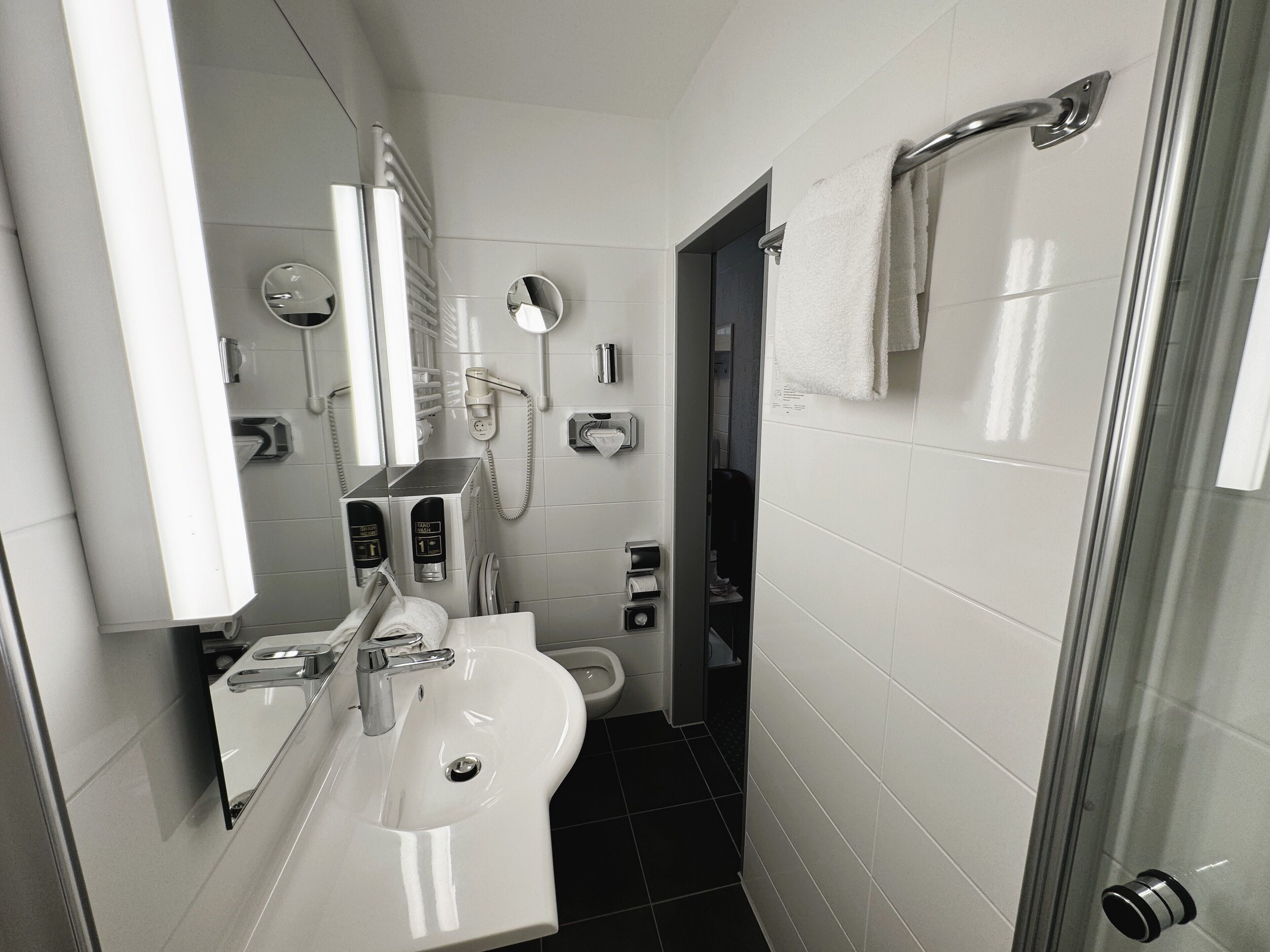 A modern bathroom with a sink, mirror, towel rack, and a shower area.