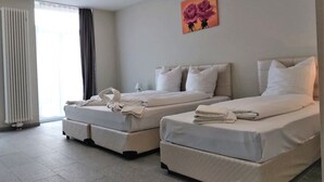 Ein Hotelzimmer mit zwei Betten, einem Heizkörper, einem Fenster mit Vorhängen und einem Blumenbild an der Wand.