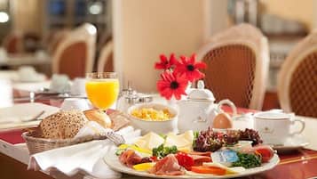 A breakfast setting with a variety of food items, including bread, eggs, and vegetables, on a table with chairs and a vase of flowers.