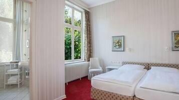 Een hotelkamer met een groot bed, een radiator, een stoel en een raam met gordijnen.