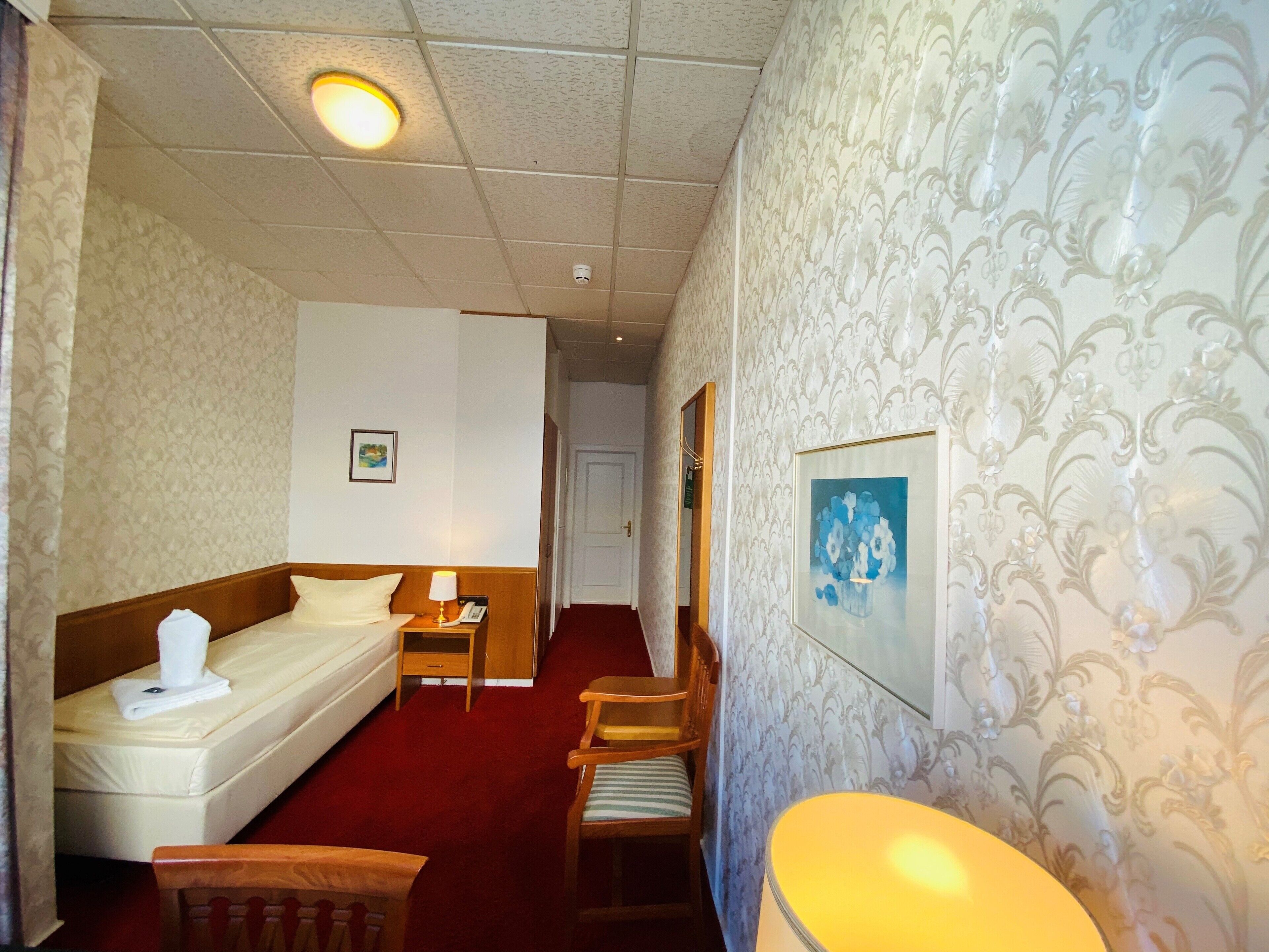 Ein Hotelzimmer mit Bett, Nachttisch mit Lampe, einem Sessel und einem gerahmten Bild an der Wand.