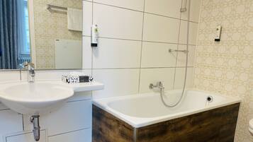 A bathroom with a sink, mirror, and a bathtub with a wooden base.