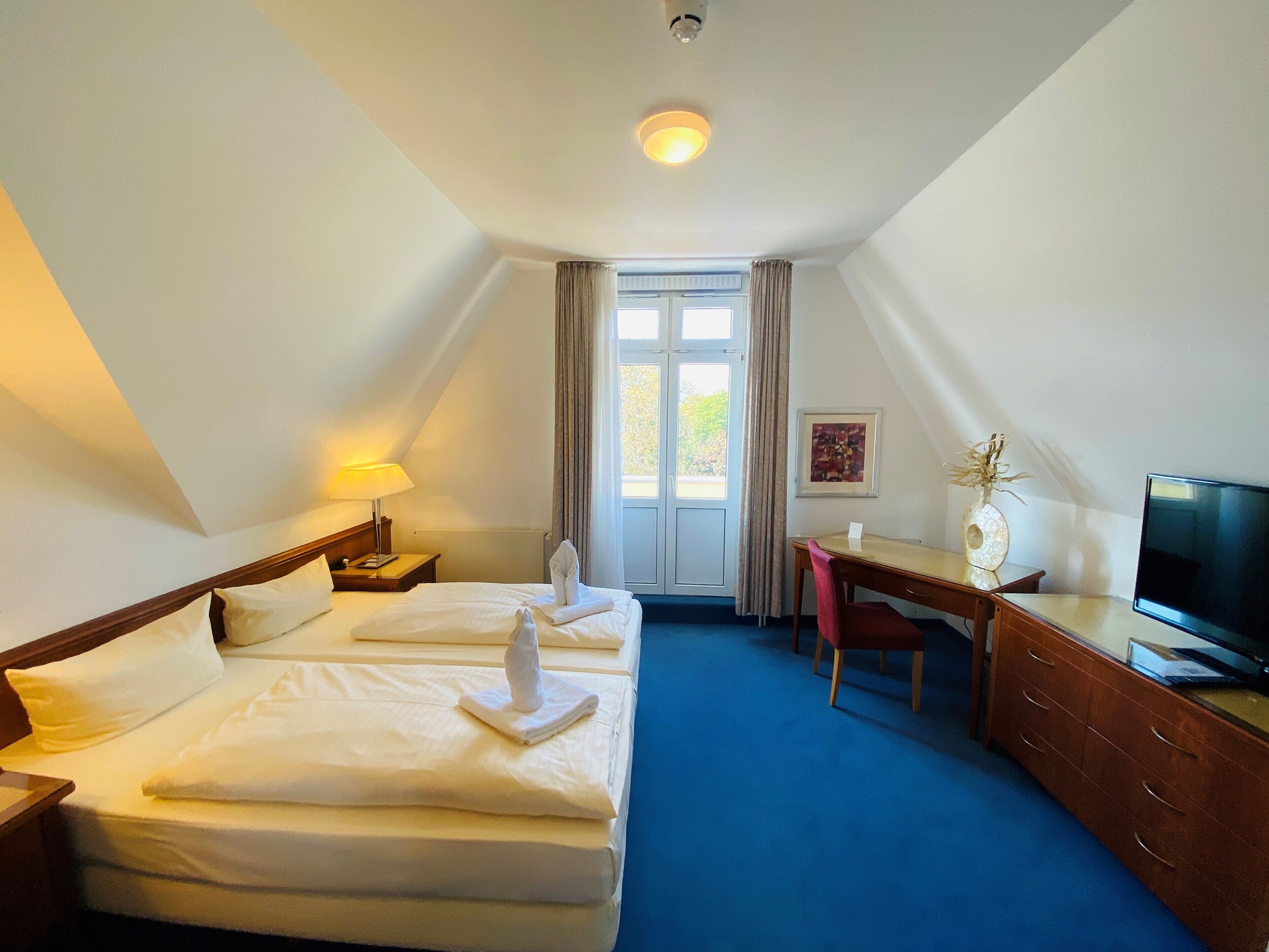 A hotel room with two beds, a desk, a chair, a television, and a window with curtains.