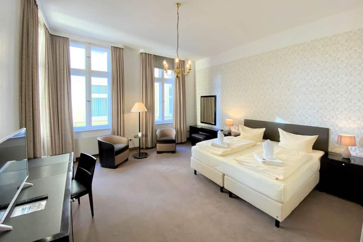 A hotel room with a bed, desk, chairs, and a chandelier.