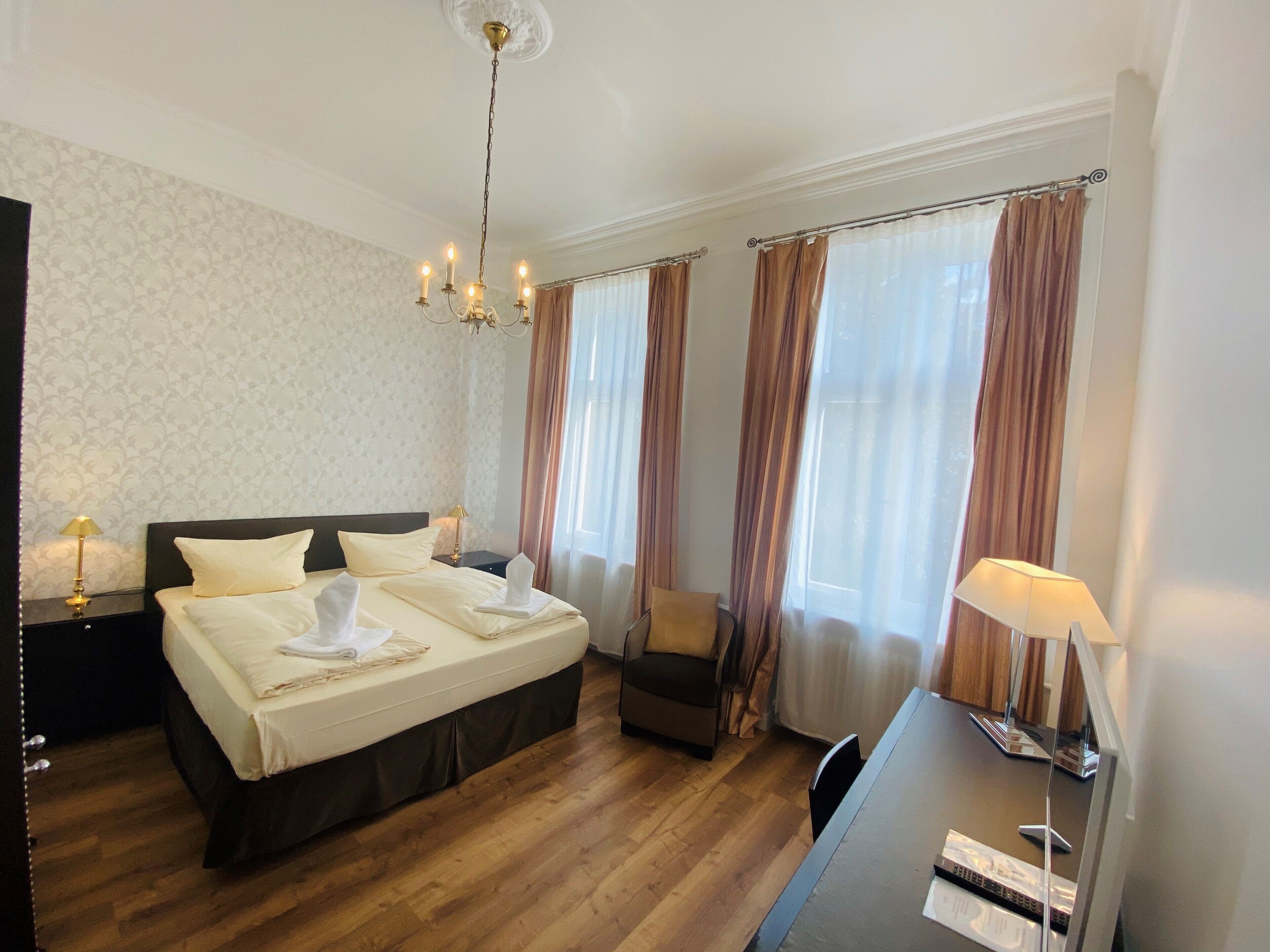 Una camera d'albergo con un letto grande, una scrivania, una sedia, un lampadario e tende.