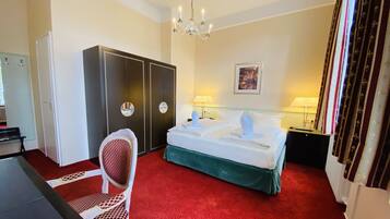 A hotel room with a bed, a desk, a chair, a wardrobe, and a chandelier.