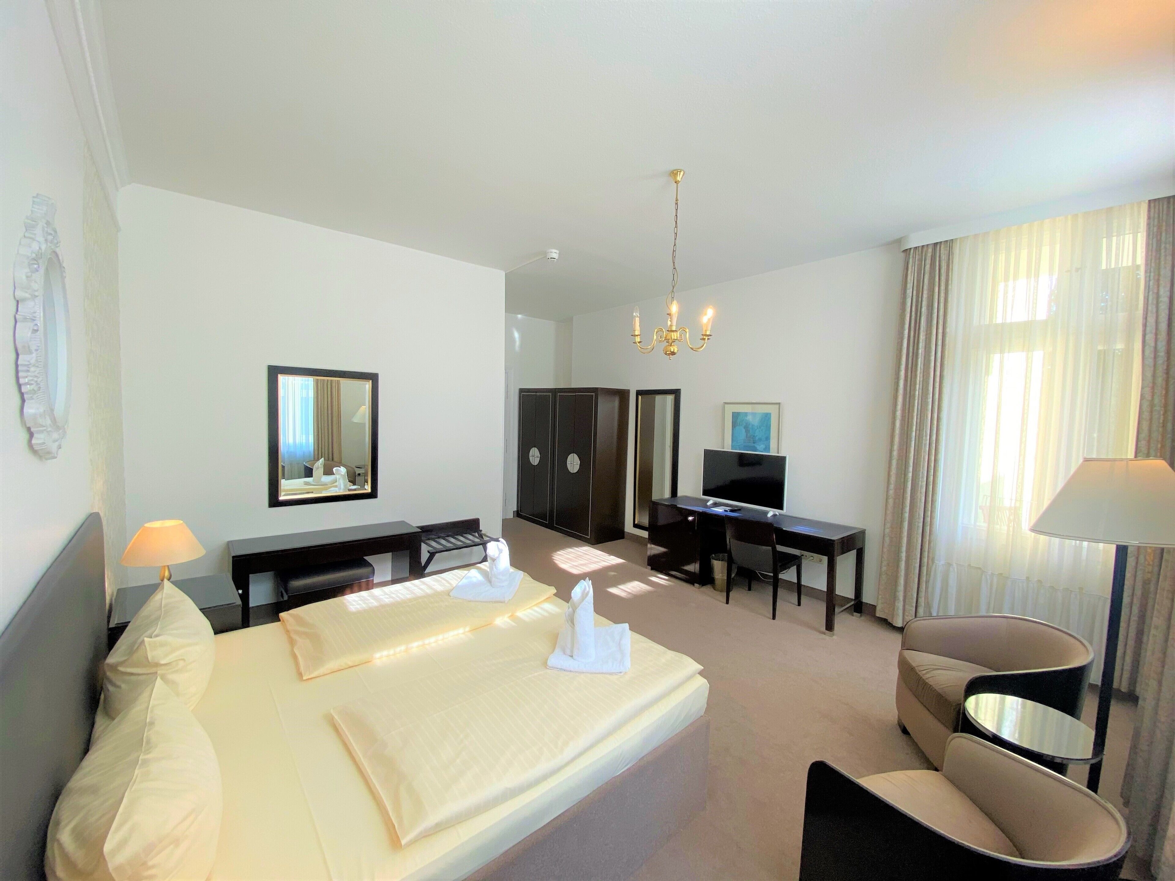 Une chambre d’hôtel avec un lit double, un bureau avec un ordinateur, une télévision, une chaise et un lustre.