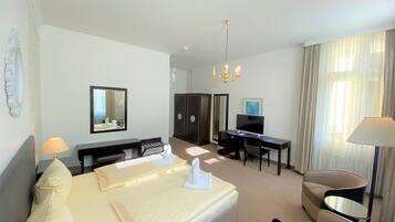 Une chambre d’hôtel avec un lit double, un bureau avec un ordinateur, une télévision, une chaise et un lustre.