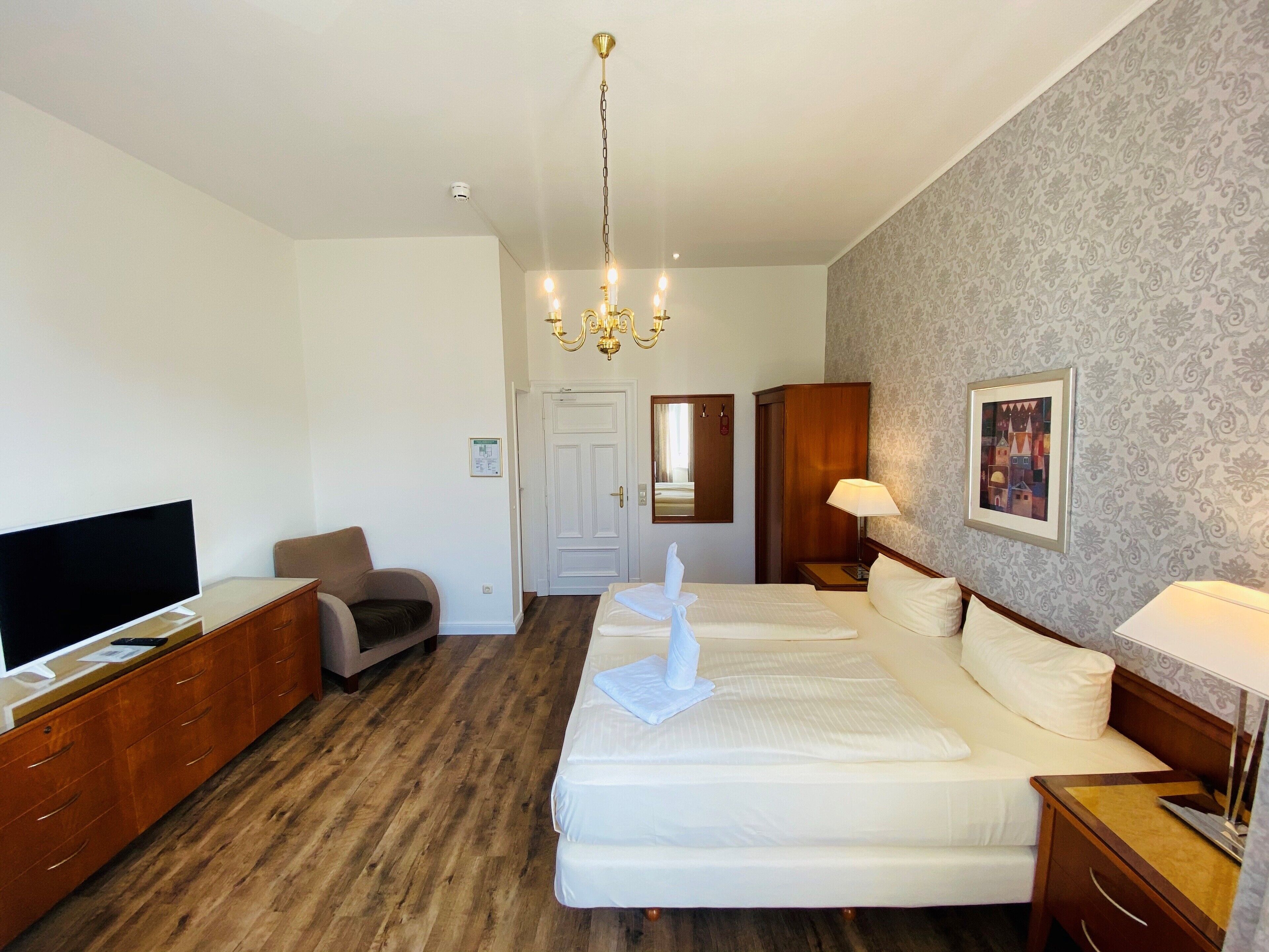 Ein Hotelzimmer mit einem großen Bett, einem Fernseher, einem Schreibtisch, einem Stuhl, einem Kleiderschrank und einer Kandelaber.