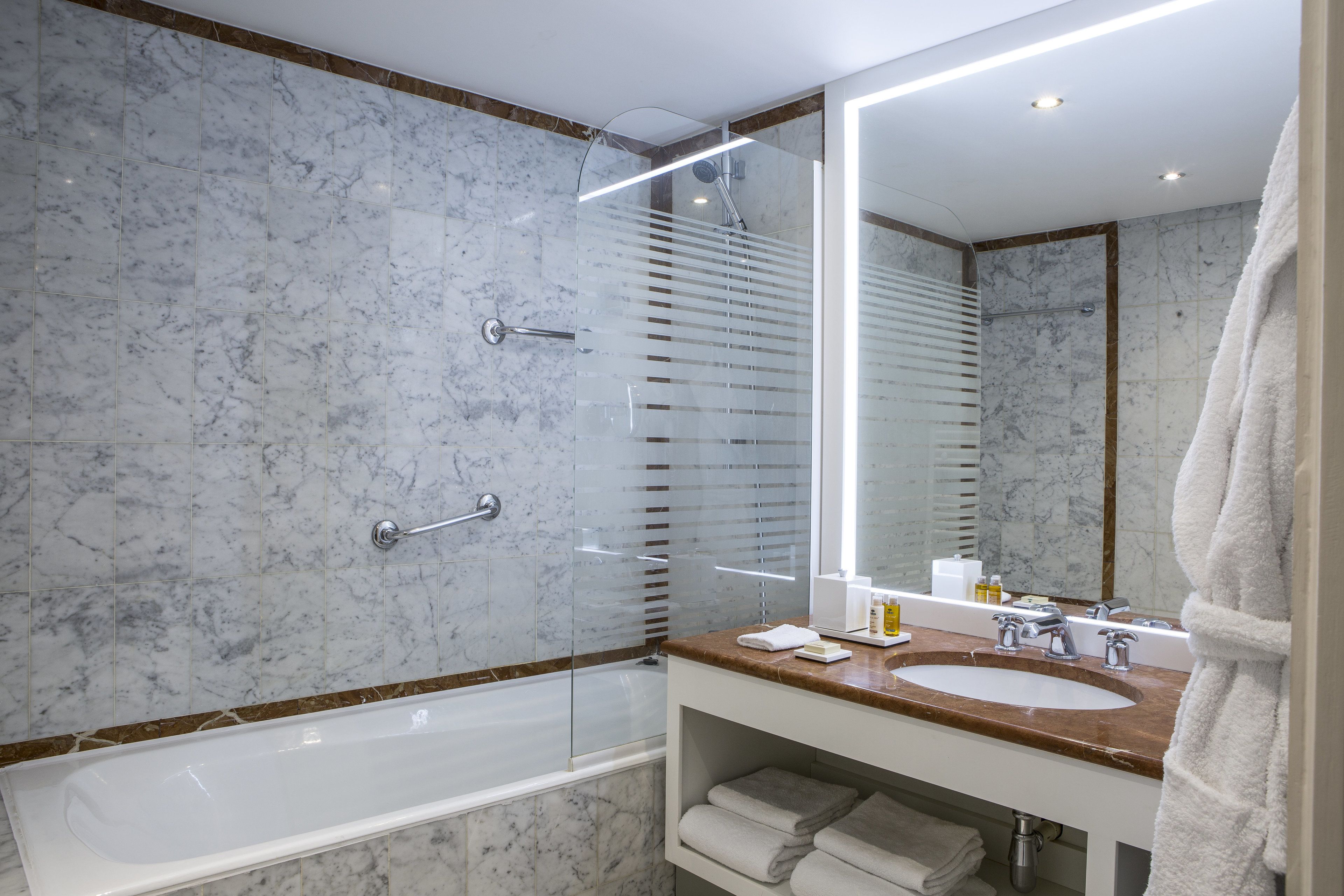 A modern bathroom with a marble wall, a glass-enclosed shower, a sink with a vanity, and a large mirror.