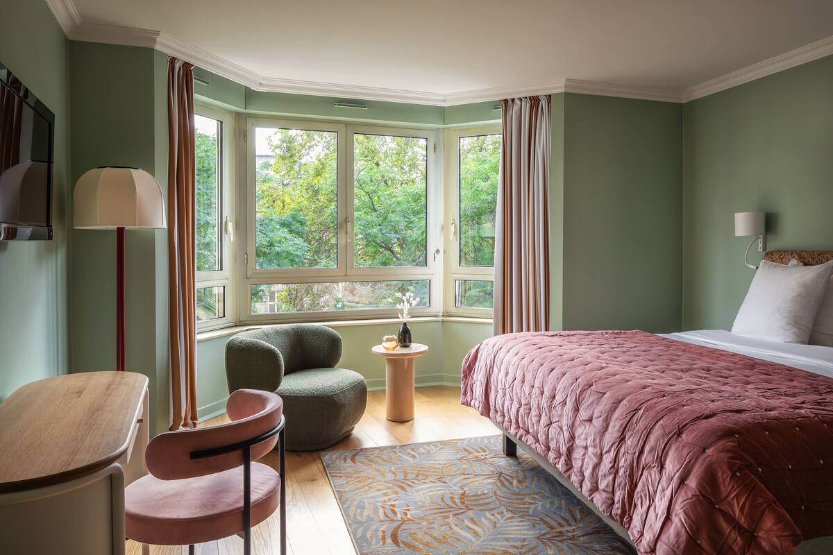 Une chambre à coucher avec un lit, une chaise, une table et une fenêtre avec des rideaux.