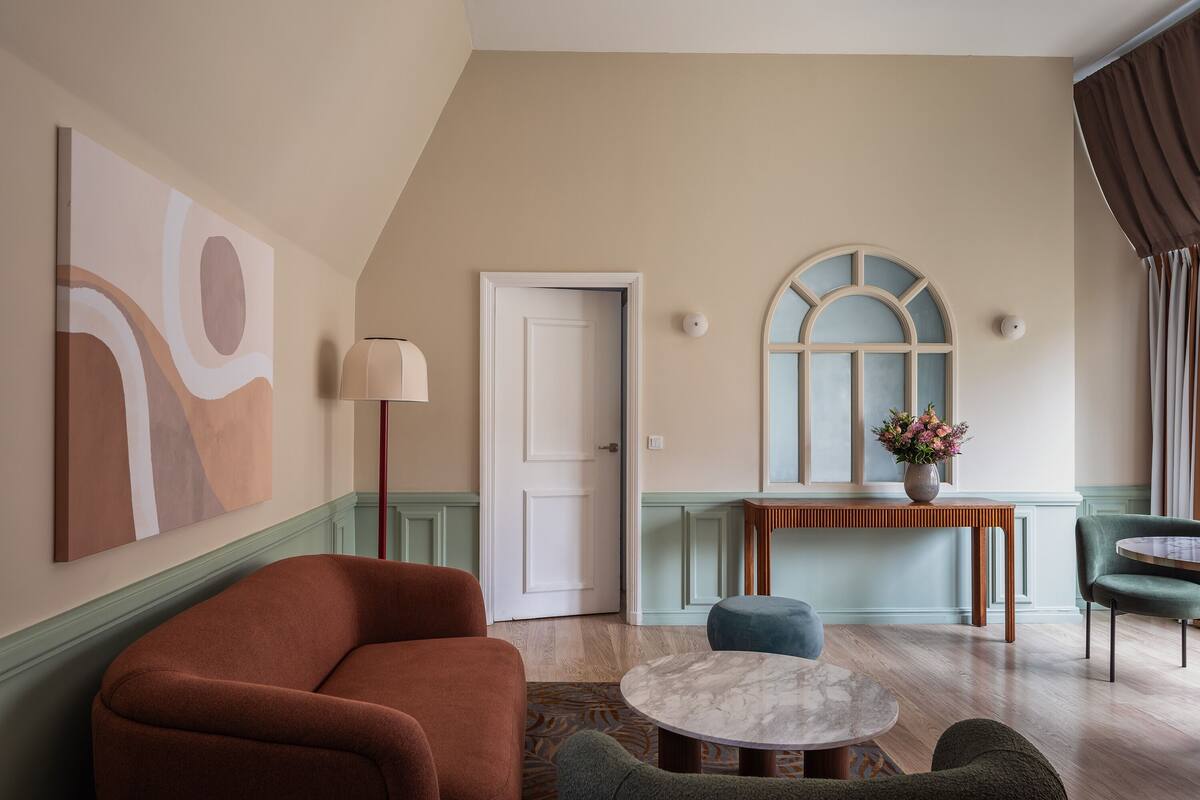 Une pièce comprenant un grand tableau abstrait, une table ronde en marbre et un fauteuil recouvert d’un tissu vert.