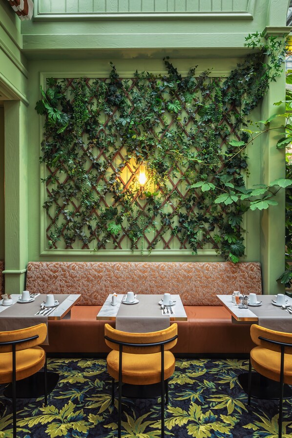 Un restaurant doté d’un mur végétal recouvert de lierre, d’un banc en bois et de chaises jaunes.