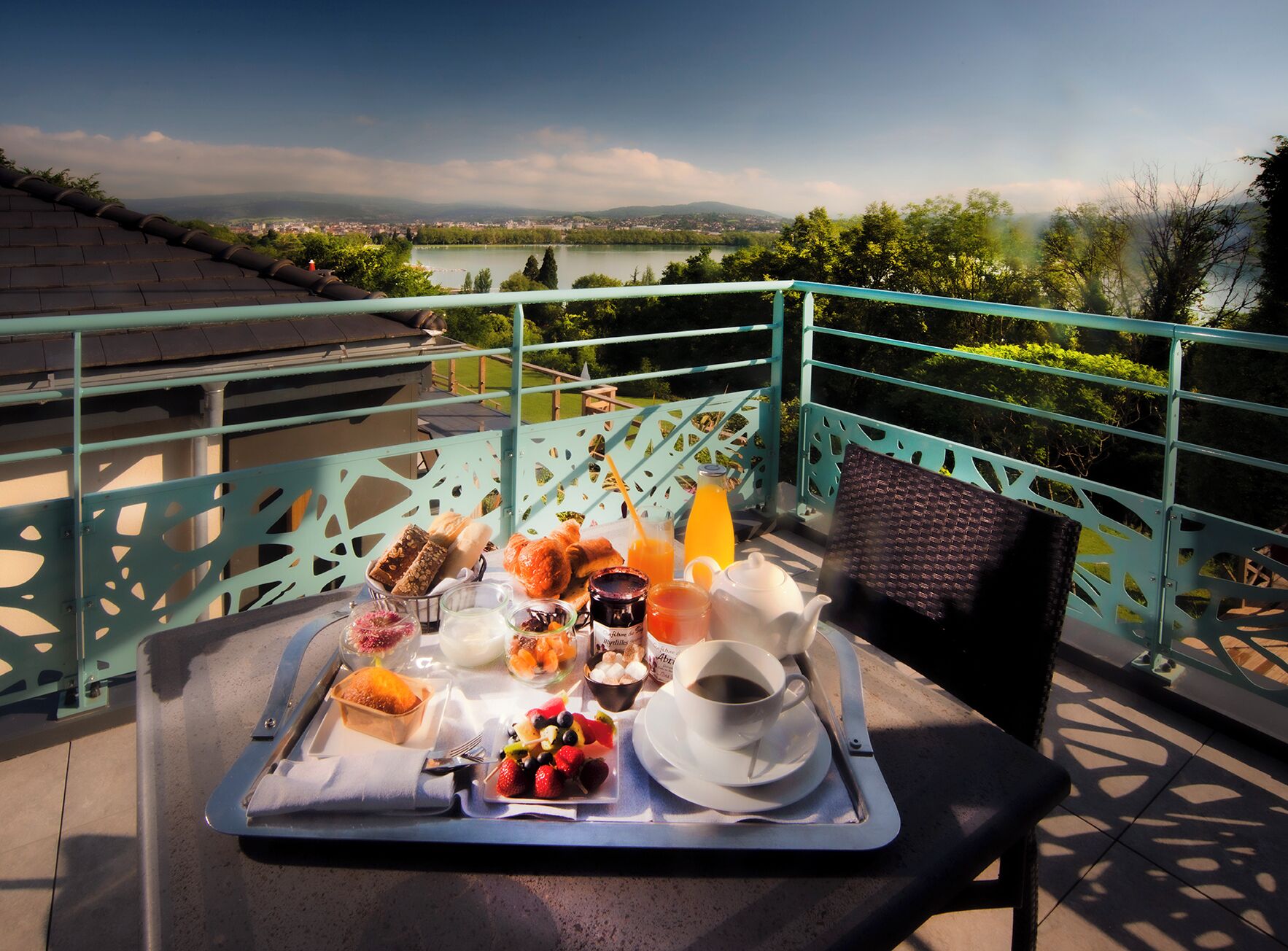Bandeja de desayuno en un balcón con vistas panorámicas a un lago y montañas.