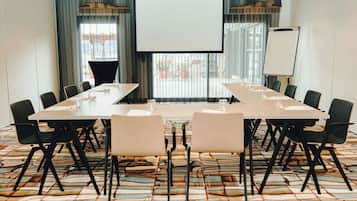 Un salón de conferencias con una gran mesa, sillas, una pantalla de proyector y una pizarra.