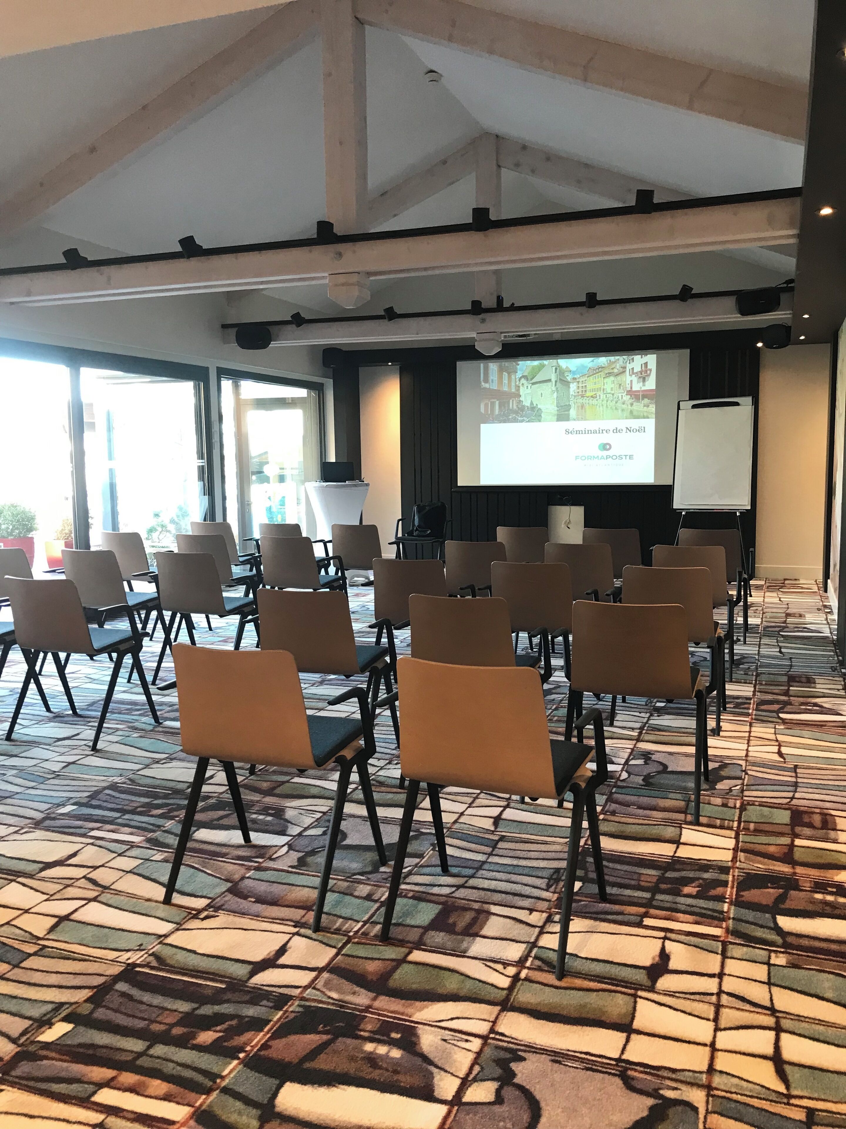 Un salón de conferencias con filas de sillas, una pantalla de proyector y una pantalla para presentaciones.
