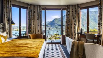 Una habitación de hotel con una cama grande, un sofá, un balcón y vistas a montañas y un lago.