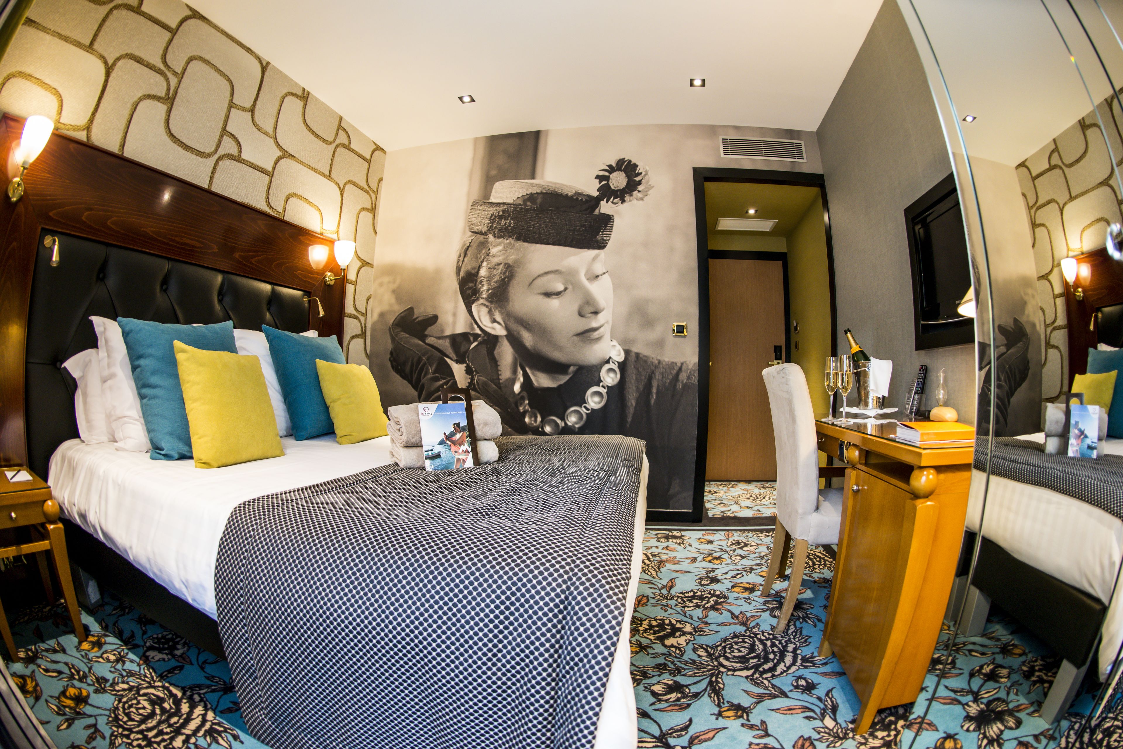 Una habitación de hotel con una cama grande, una mesita de noche de madera, un escritorio y un espejo.