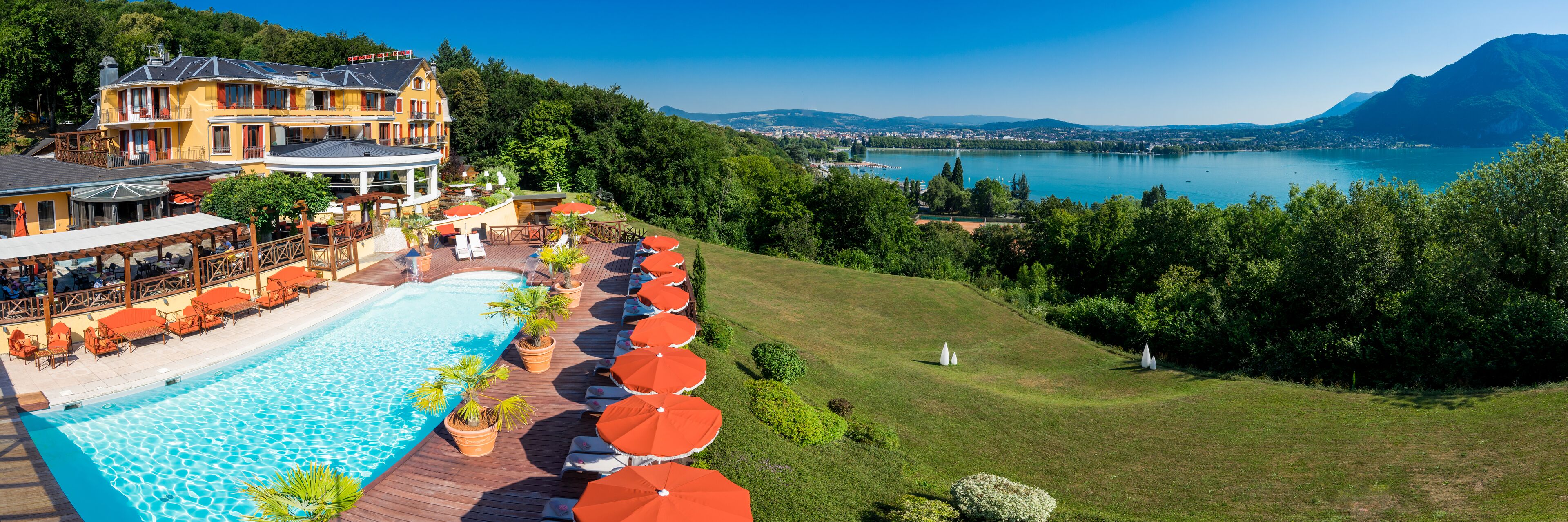 Un resort con piscina, mobiliario exterior y vistas a un lago y montañas.