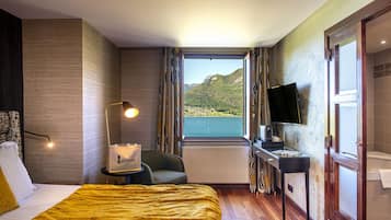 Une chambre d’hôtel équipée d’un lit, d’un bureau, d’une chaise, d’une télévision et d’une fenêtre donnant sur les montagnes.