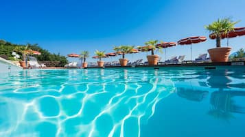 Relax by the serene pool surrounded by lush greenery and lounge chairs.