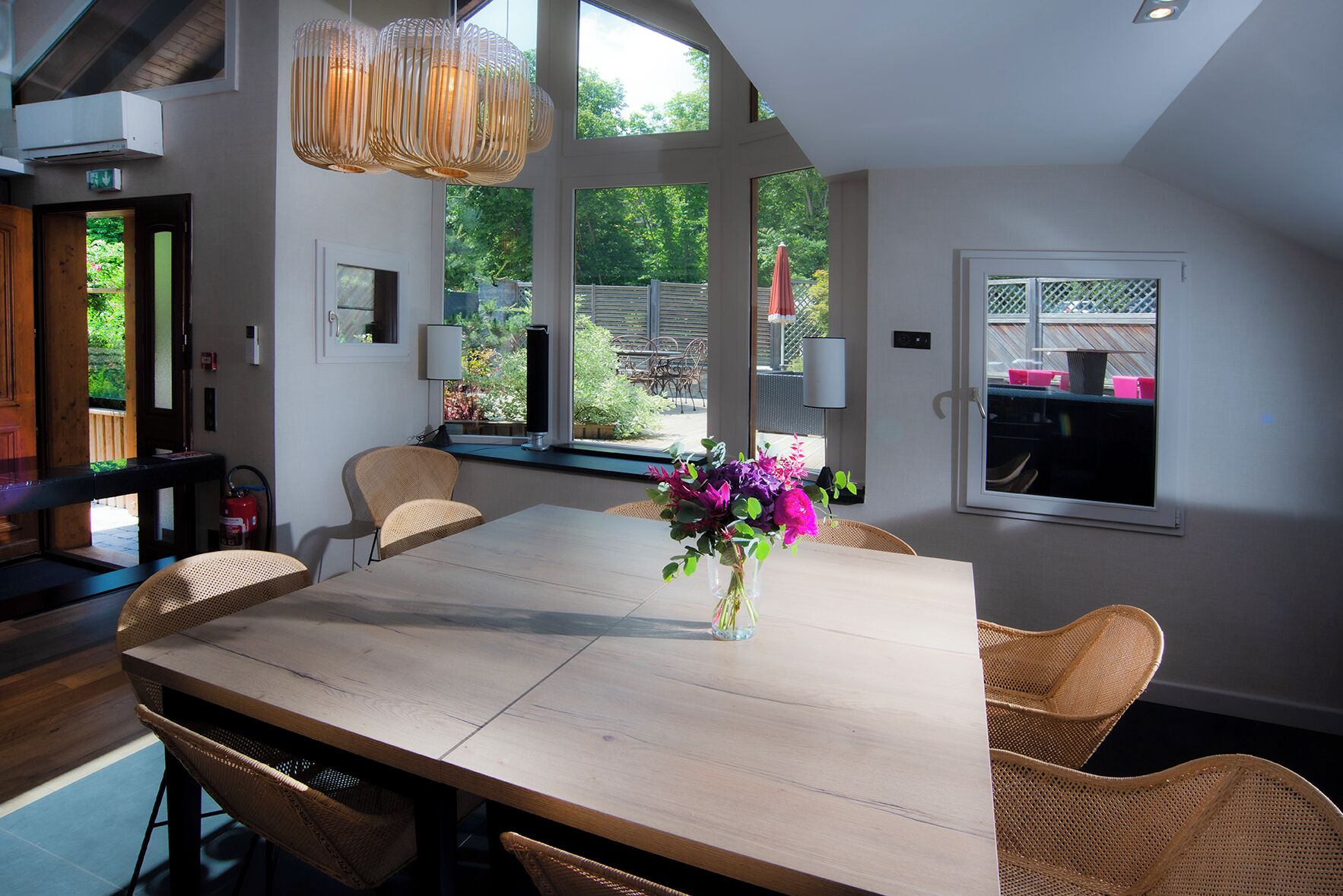 Un coin repas avec une table en bois, des chaises en osier et un vase de fleurs.
