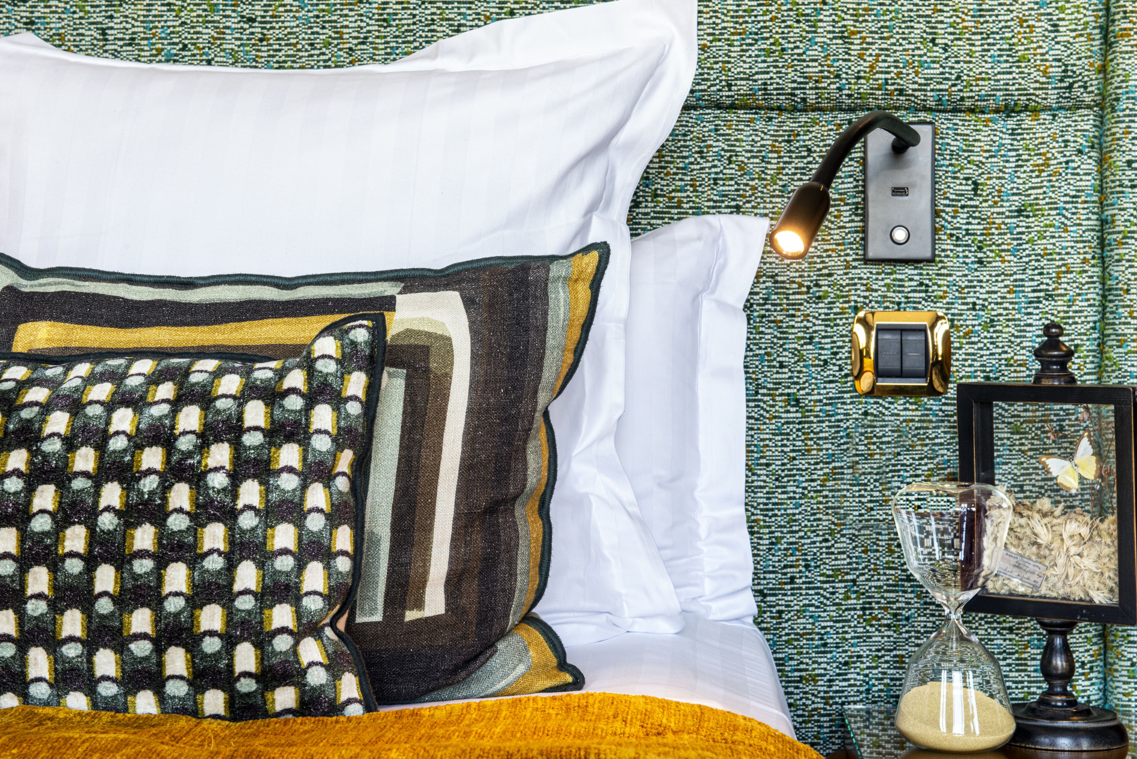 A neatly made bed with patterned pillows and a bedside table with a lamp, clock, and decorative items.