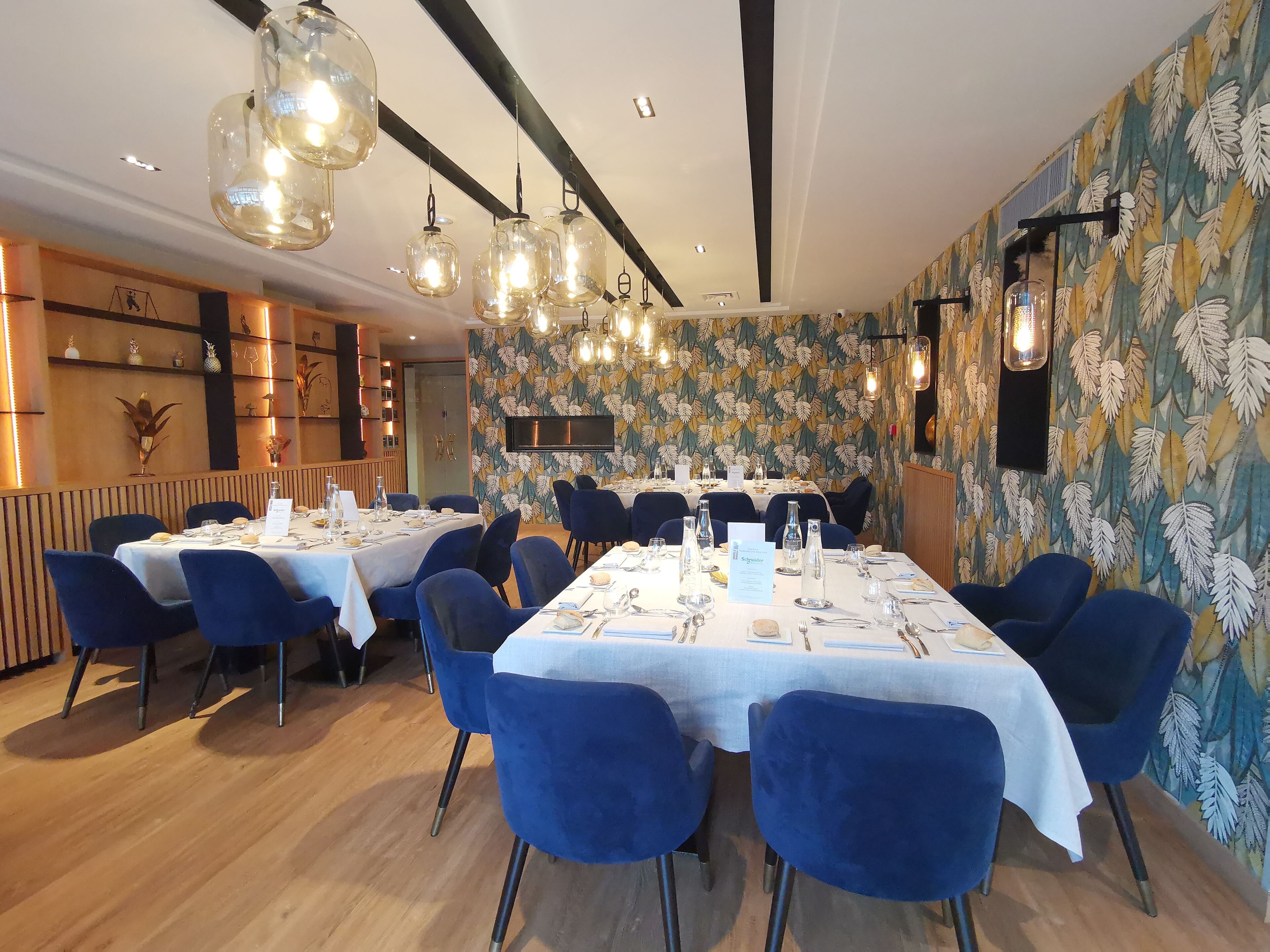 Un restaurante con una larga mesa dispuesta para comer, sillas azules y lámparas colgantes.